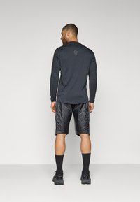 T-shirt de sport noir à manches longues avec des manches contrastées, associé à un short noir brillant. Design simple avec des accents zippés à l'ourlet.
