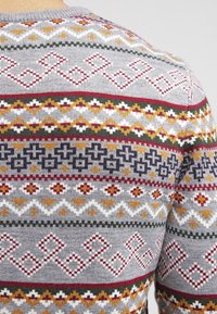 Maglione grigio lavorato a maglia con motivi geometrici multicolori in rosso, verde, giallo e bianco sulla schiena. Collo rotondo, texture morbida.