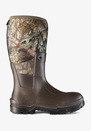 Brown rubber boot featuring a camo textile upper with leaf and branch patterns, textured side panel, and a thick black traction sole.