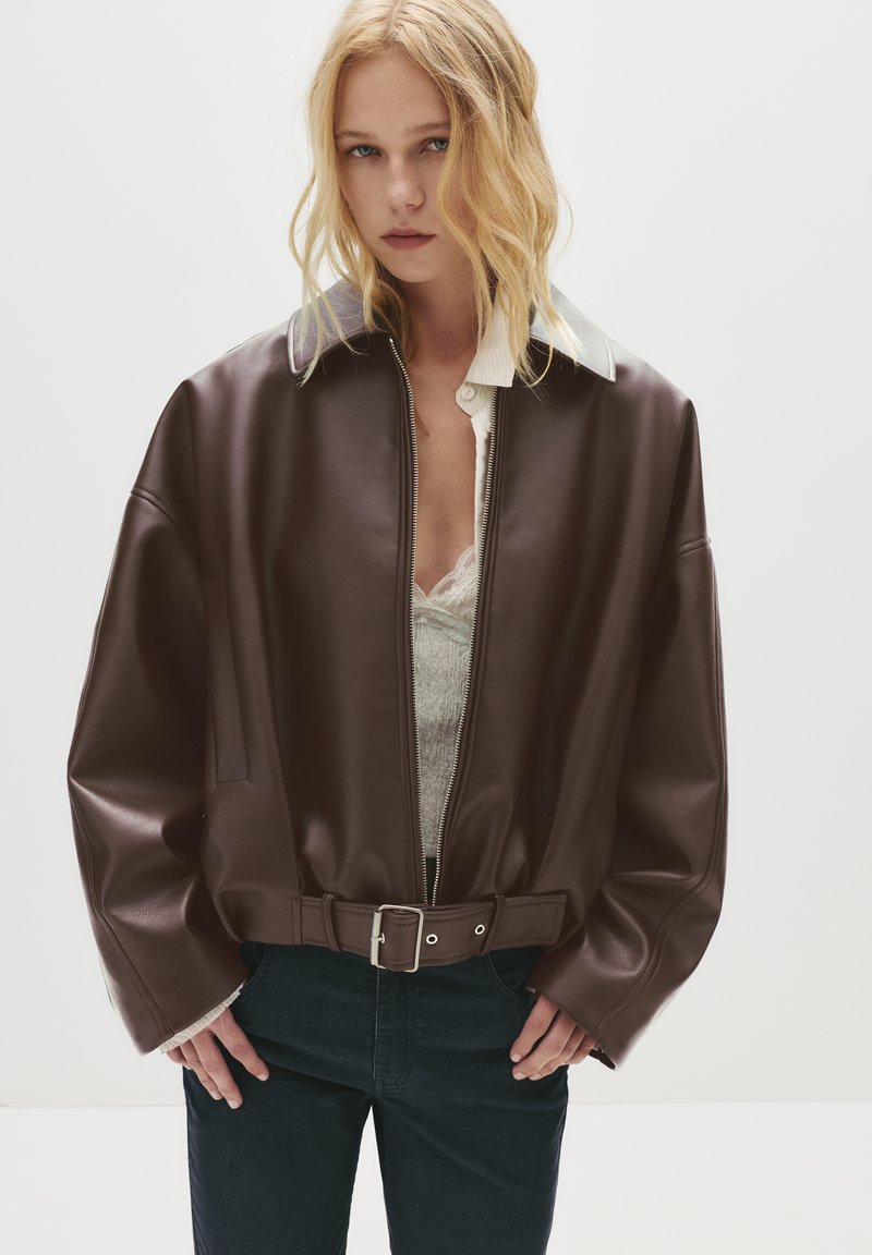 Giacca bomber in finta pelle marrone con chiusura a zip, colletto ampio e vita con cintura. Presenta maniche larghe e rilassate e una texture liscia.