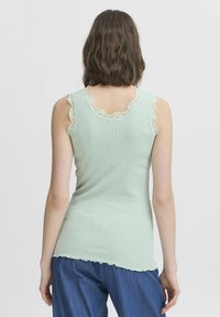 Ribidega helesinine tank top, mille krae ja käeaugud on pitsiga kaunistatud. Ümar hemline lainelise äärisega. Näidatud tagakülje vaade.