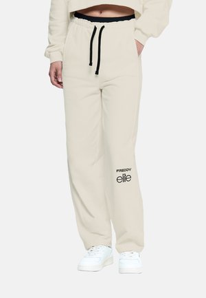 Pantalones de chándal color crema con cintura elástica y cordón negro, que presentan un logo impreso en negro en el muslo. Hechos de material suave.