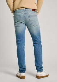 Vaqueros de mezclilla azul claro con un diseño ajustado. Las características incluyen dos bolsillos traseros, un sutil desgaste y una parche de cuero marrón en la cinturilla.
