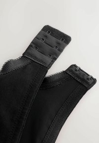 Gros plan sur des bretelles de soutien-gorge noires avec fermeture à agrafes comportant trois rangées de crochets sur un tissu texturé en mesh et élastique.