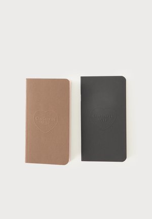 To lukkede notesbøger side om side, en brun og en sort, begge med et hjerteformet præget logo med teksten "Carhartt WIP" på omslaget.