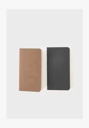 Dwa zamknięte notesy obok siebie, jeden brązowy, drugi czarny, oba z wytłoczonym logo w kształcie serca z napisem "Carhartt WIP" na okładce.