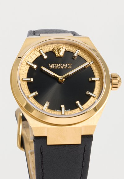 Χρυσό ρολόι Versace με μαύρο καντράν, χρυσούς δείκτες ώρας, έμβλημα κεφαλής Μέδουσας στις 12 η ώρα και μαύρο δερμάτινο λουράκι.