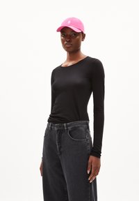 Schwarzes Langarmshirt, kombiniert mit hochgeschnittenen, dunkelgrauen Jeans. Eine rosa Kappe mit Logo rundet das Outfit ab. Einfaches und modernes Design.