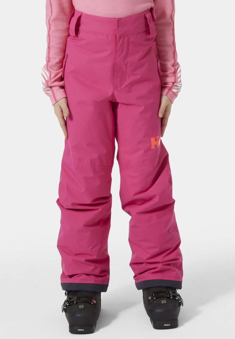 Světlé růžové lyžařské kalhoty vyrobené z voděodolného materiálu, s volným střihem, bočními kapsami a logem v oranžové na koleni.