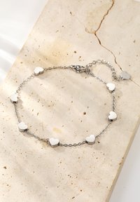 Silver chain bracelet featuring alternating shiny heart-shaped charms, smooth texture, and a lobster clasp, displayed on a light stone surface.