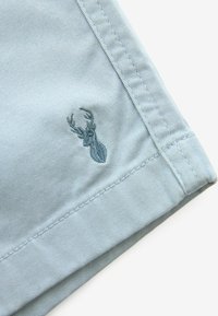 Țesătură din bumbac de culoare albastru deschis, cu o textură netedă, având un logo de cerb brodat pe margine, accentuat de o cusătură curată.