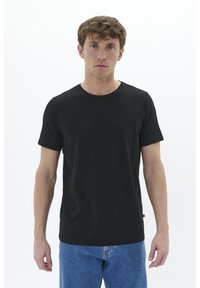 Melns īsām piedurknēm T-krekls, izgatavots no gludas auduma, ar apaļu izgriezumu un vienkāršu dizainu. Kombinēts ar gaiši ziliem džinsiem.