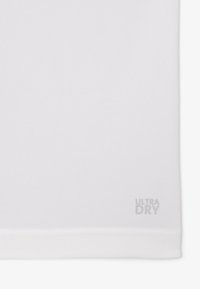 Maglietta sportiva bianca in un tessuto testurizzato e traspirante con un'etichetta sull'orlo che recita "ULTRA DRY" in grigio chiaro. Design semplice, senza motivi aggiuntivi.