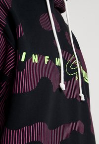 Černá mikina s kapucí s růžovým pruhovaným vzorem a velkým grafickým logem. Obsahuje stahovací kapuci a bílé detaily, což poskytuje živý design.