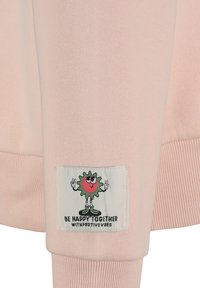 Helle rosa Sweatshirt mit gerippten Bündchen, ausgestattet mit einem dekorativen Patch, der eine Cartoonfigur und den Text "SEI GLÜCKLICH ZUSAMMEN MIT POSITIVEN VIBES" zeigt.