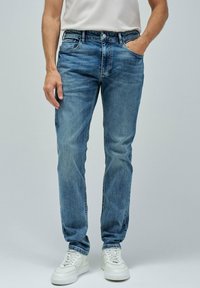 Vaqueros de mezclilla azul con un corte recto, diseño de cinco bolsillos y un ligero desgaste, combinados con zapatillas blancas.