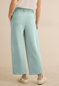 Pantalons larges bleu clair avec une texture lisse et une taille élastique, dotés de deux poches arrière et associés à des baskets blanches.