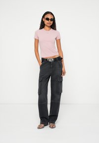 Ροζ εφαρμοστή μπλούζα με λογότυπο, συνδυασμένη με μαύρο παντελόνι καμπαρντίνας με πλαϊνές τσέπες, φορεμένη με μαύρη ζώνη και σανδάλια.