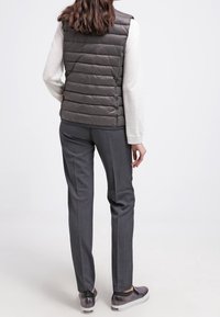 Gilet grigio in piuma con cuciture orizzontali, indossato sopra un maglione chiaro, abbinato a pantaloni grigi su misura e scarpe slip-on testurizzate.