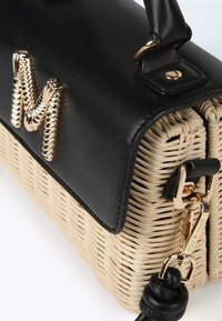 Black faux leather top with gold "M" accent, woven natural straw body, gold hardware, and detachable black strap. Structured rectangular shape.