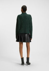 Grön stickad tröja med ribbad textur, med hög krage, kombinerad med en svart läderplisserad kjol och ankelstövlar.