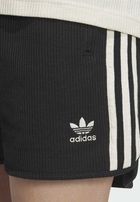 Černé žebrované šortky s bílými bočními pruhy, na levé noze mají vyšitý bílý logo Adidas. Lehká textilie.