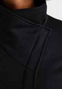 Zwarte hoge hals kleding met een gladde, gestructureerde afwerking. Beschikt over een stijlvolle, gevouwen kraag en een getailleerde silhoeët, die de strakke lijnen benadrukt.