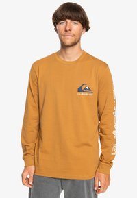Long-sleeve shirt in mustard yellow cotton, featuring a blue logo on the chest and white text along the left sleeve for branding.