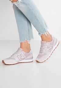 Helle rosa Wildledersneaker mit weißen Akzenten und einer strukturierten Gummisohle, die über durchbrochene Details und ein klassisches New Balance-Logo verfügt.