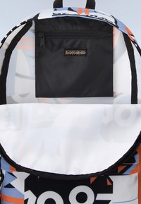 Un sac à dos avec une poche zippée noire, un motif géométrique coloré, un intérieur blanc et bleu, un tissu doux et des bretelles noires ajustables.