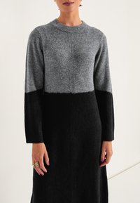 Neulepuku, jossa on harmaa yläosa ja musta alaosa, jossa on pyöreä kaula-aukko ja pitkät hihat. Pehmeä rakenne, suora siluetti, minimaalinen koristelu.