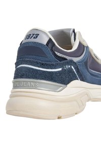 Dark blue sneaker with a textured suede and mesh upper, cream accents, and a chunky rubber sole. Features branding on the heel.
