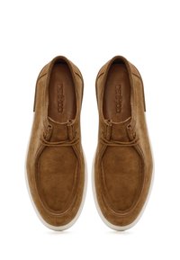 Chaussures slip-on en suede marron avec une texture lisse, bout arrondi et semelle en caoutchouc blanche. Présente une couture minimale et un simple accent de lacet.