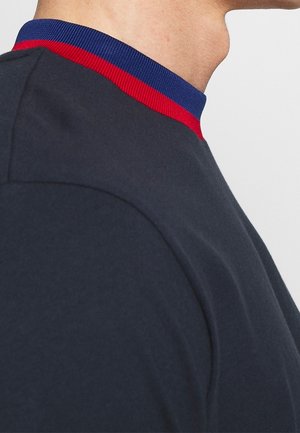 Felpa blu navy con collo a costine caratterizzato da strisce rosse e blu. Tessuto morbido, design aderente che mette in risalto la cucitura delle spalle.