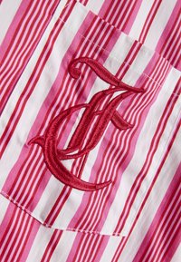 Tkanina s črtami v roza in beli barvi z žepom, na katerem je rdeče vezena črka "F." Tekstura je gladka, s vidnimi šivnimi podrobnostmi.