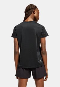 T-shirt de sport noir à manches courtes, fabriqué à partir d'un tissu léger et évacuant l'humidité. Présente un accent de logo en bas à droite.