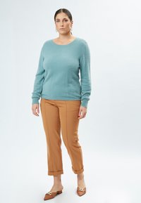 Lyseblå, fluffy sweater med lange ærmer og rund halsudskæring. Sammen med lysebrune, skræddersyede bukser med sidesøm og opsmøg.