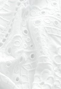 Vit broderad tyg med intrikata mönster och cirkelformade utskärningar samt texturerad sömnad. Mjukt, lätt material.