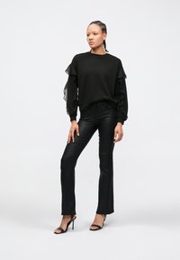 Zwarte pullover trui met gerimpelde doorschijnende mouwen, gecombineerd met nauwsluitende zwarte uitlopende broek en zwarte sandalen met hoge hakken. Eenvoudig ontwerp.