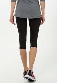 Czarne legginsy capri z elastycznego materiału, noszone z szarym topem i czarnymi sneakersami. Charakteryzują się dopasowanym krojem i skróconym fasonem, odsłaniającym kostki.