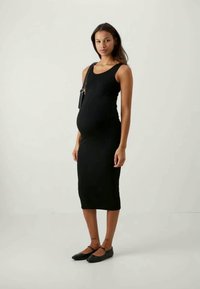 Μαύρο, εφαρμοστό midi φόρεμα με αμάνικο σχέδιο, μαλακή υφή και ήπια καμπυλωτή λαιμόκοψη, που φοράει μια έγκυος μοντέλο.