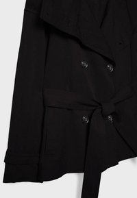 Trench coat nero doppiopetto con ampi revers, quattro bottoni, maniche lunghe, cintura annodata in vita e tasche laterali.