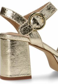 Sandalias de plataforma metálicas doradas con un acabado texturizado, amplias correas cruzadas y un gran acento circular en el tobillo.