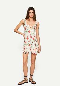 Rochie florală cu bretele volanate și un detaliu în formă de cheie. Material bej deschis cu trandafiri roșii și frunze verzi. Fustă scurtă, evazată.