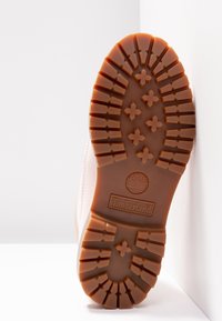 Semelle de chaussure Timberland, présentant un design robuste en caoutchouc brun avec des motifs croisés pour l'adhérence et un logo central.