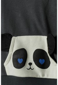 Primo piano di un tessuto grigio con una tasca bianca progettata come un volto di panda, caratterizzata da orecchie nere e macchie per gli occhi con pupille a forma di cuore blu.