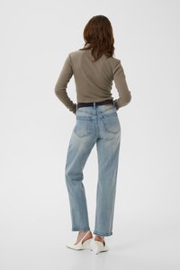 Lyseblå jeans med rette ben og falmede områder, midt på livet, synlige baklommer, kombinert med en langermet topp i taupefarge og hvite hæler.