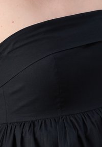 Robe noire sans bretelles en tissu mat et lisse ; comporte un corsage ajusté et une jupe plissée créant une silhouette fluide.