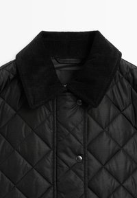 Zwarte doorgestikte jas met een corduroy kraag, drukknoopsluiting en een gladde textuur, waarbij een diamantpatroon op de stof wordt benadrukt.