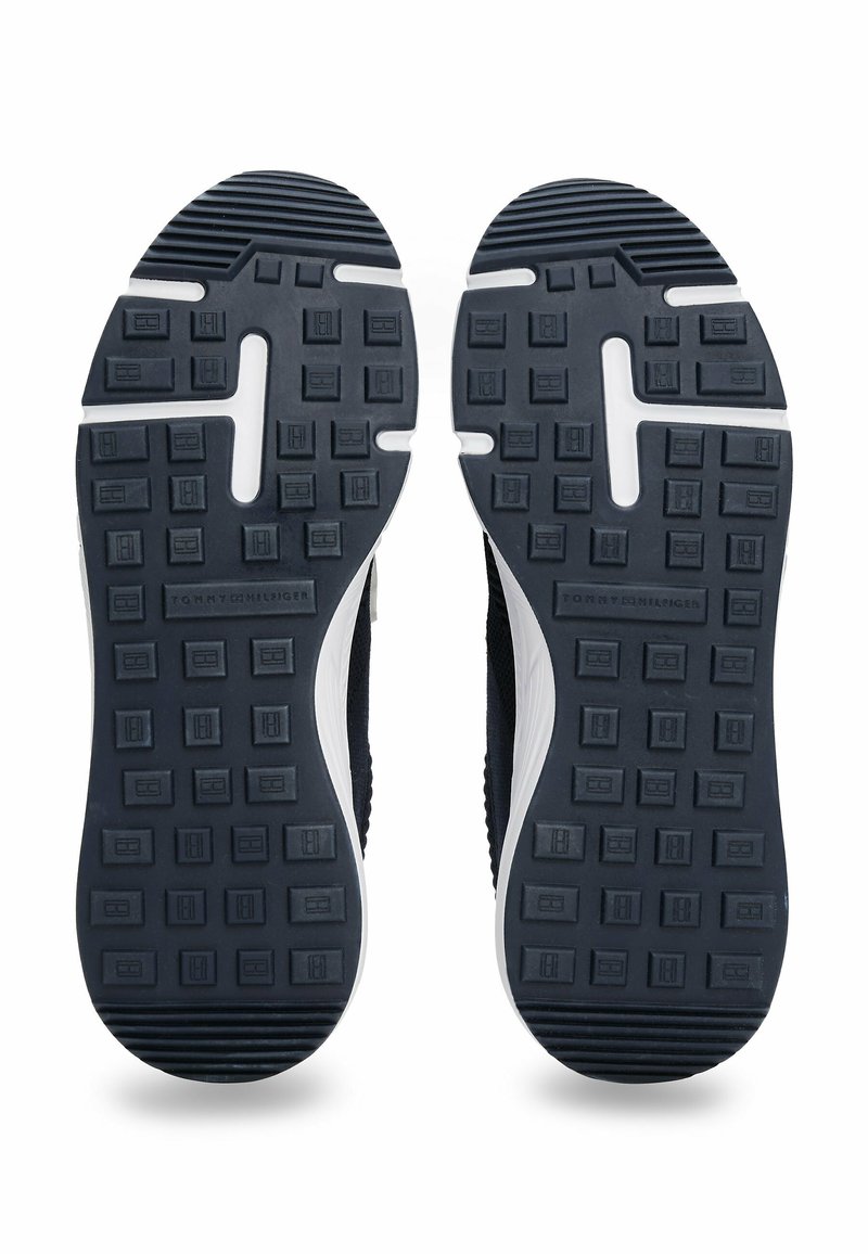 Suelas de sneakers azul marino con goma texturizada para mejor agarre, que presentan una entresuela blanca y un detalle de logo en relieve. Patrones de tracción cuadrados y rectangulares.